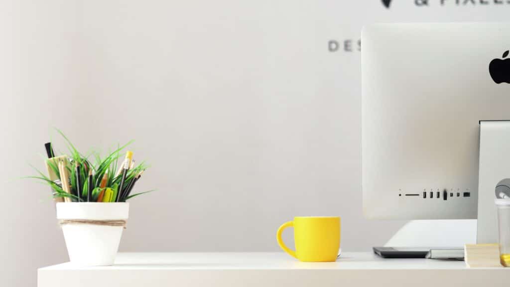 Desk with bright yellow mug and green plants. Workplace wellness with added green space to office.